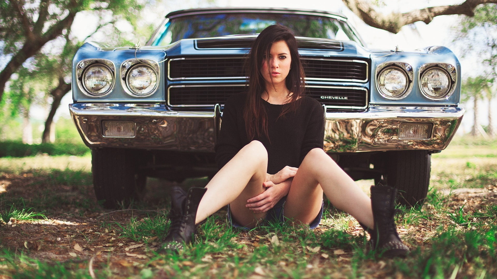 woman sitting on ground in front of blue Chevrolet Camaro