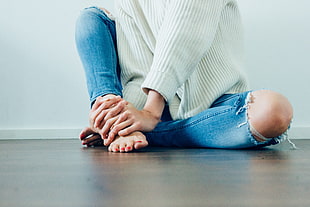 sitting person wearing white sweatshirt and distressed blue jeans