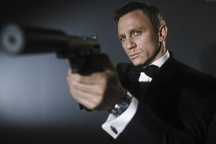 man in black suit jacket holds a semi-automatic pistol