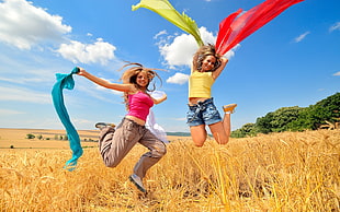 two women in clothing jumping on brown grass field during daytime