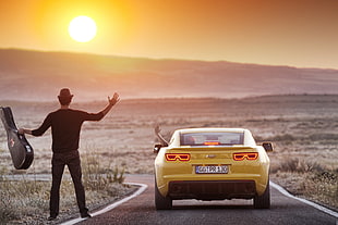 man holding guitar case waving at yellow car at the desert during sunset HD wallpaper