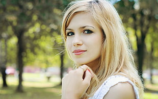 selective focus photography of woman in white sleeveless top and blond hair near trees during daytime