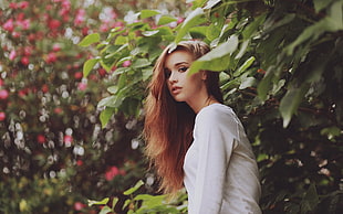 woman wearing white long-sleeved shirt surrounded by green plant