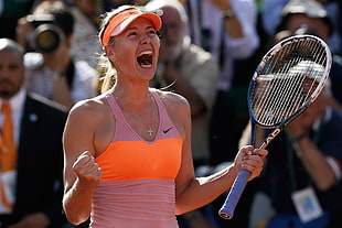 woman in orange and pink Nike tank top holding blue tennis racket