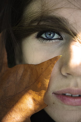 close-up photo of woman with dried leaf at her face