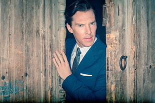 man in blue blazer beside brown wooden door