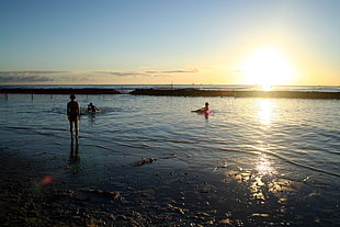 three person swimming on body of water photo during sunset day