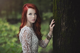 red hair woman in white lace dress stand beside tree