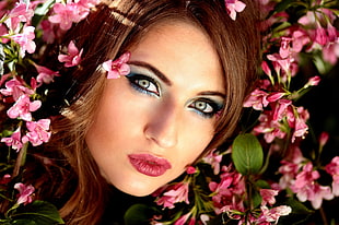 woman with red lip color black mascara over pink petaled flowers