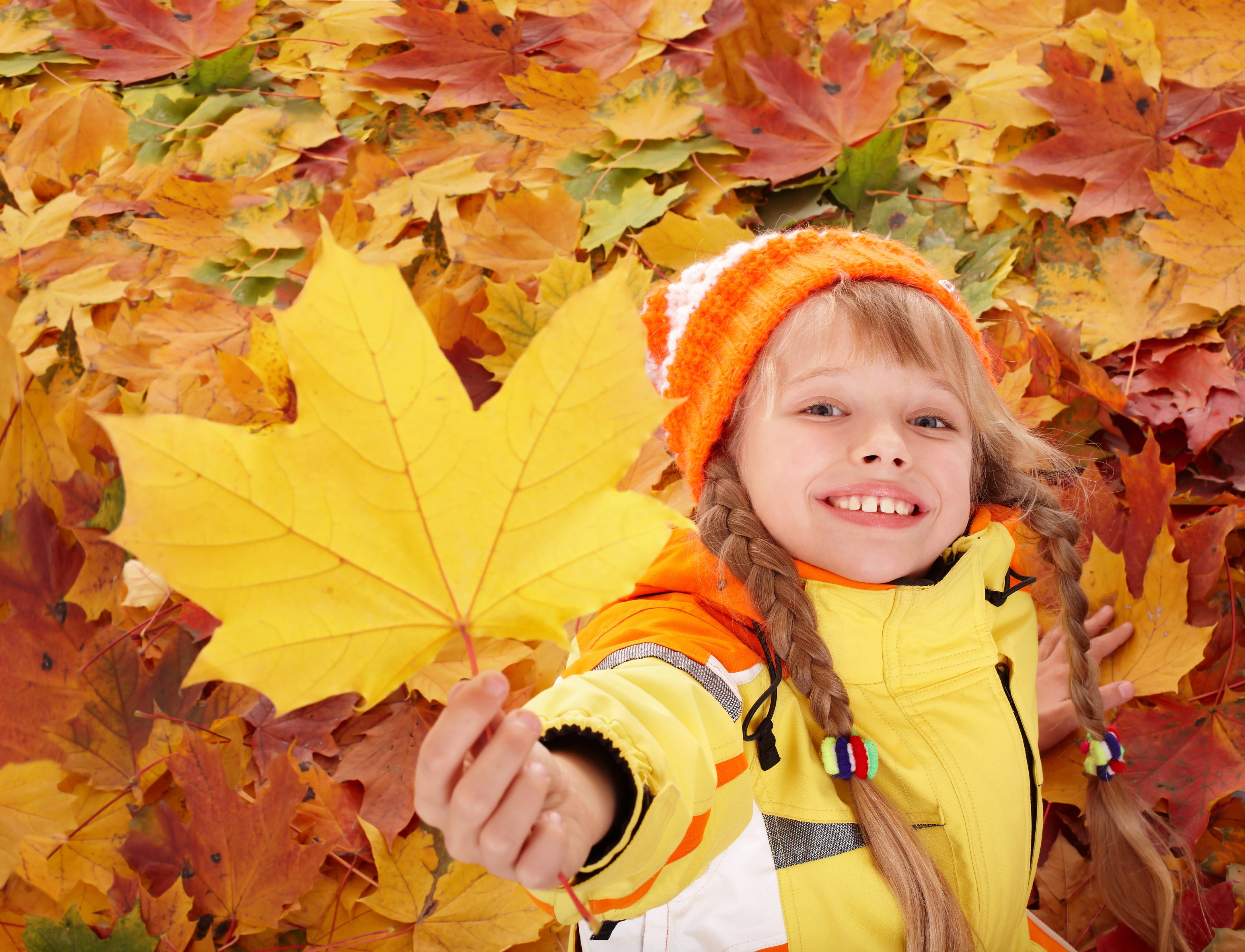 girl wearing orange knit hat and holding brown maple leaf