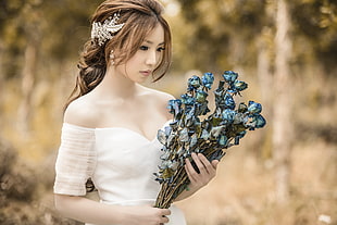 woman wearing white off-shoulder dress holding blue and gray petaled flowers