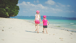 two girls walks on white sand in beach during daytime