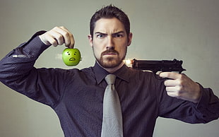 man in black dress shirt holding green apple and pistol