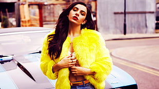 woman wearing yellow fur coat and blue denim bottoms standing beside black car