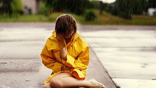 woman wearing yellow long-sleeved shirt sitting on gray concrete road while raining