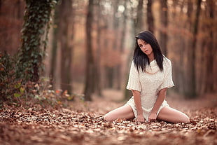 woman wearing white knitted sweater sitting on brown dry leaves during daytime