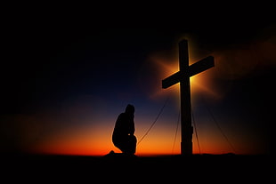 silhouette photograph of man kneeling in front of the cross