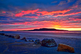 stones on brown sand near ocean during orange sunset