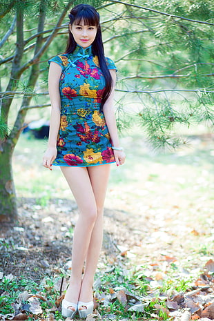woman in blue, red, and yellow floral cap-sleeved dress standing in front of green tree HD wallpaper