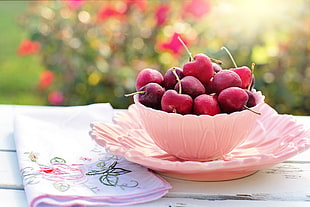 selective focus photograph of cherries on pink ceramic bowl with saucer