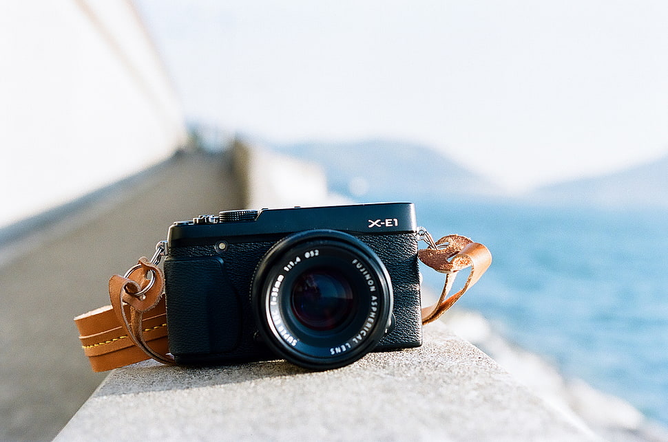 black point-and-shoot camera on gray concrete wall HD wallpaper