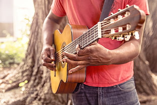 photo of man playing beige classical guitar
