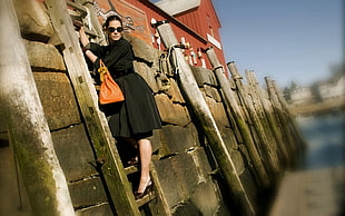 woman wearing black dress and holding bag climbing on ladder