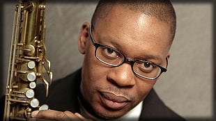 man in black framed eyeglasses holding gold plated wind instrument
