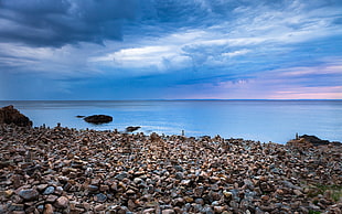 stones beside ocean under cloudy sky during daytime