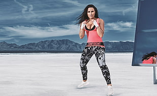 woman wearing yoga top and pants performing boxing post standing at the back of mountain cliff