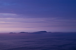 blue body of water with silhouette of island on horizon, azul