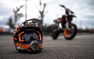 selective focus photo of orange, white, and black motocross helmet