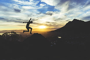 silhouette of man jumping over mountain during golden hour HD wallpaper