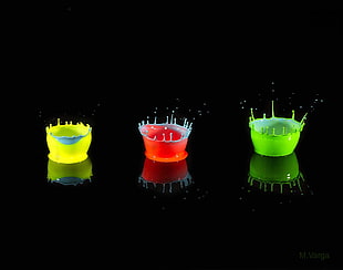 three green, red, and yellow glass candle holders, splashes, macro, colorful, black background