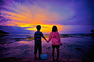 boy and girl holding each others hand while standing during sunset