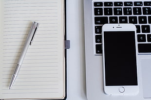 silver iPhone 6 on laptop computer and gray retractable pen on notebook