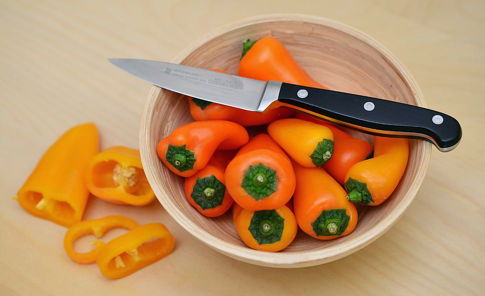 food photography of black handle kitchen knife on top of round brown bowl with a bowl of yellow bell peppers HD wallpaper
