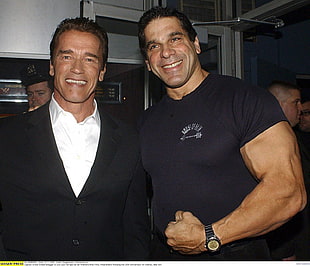 Arnold Schwarzenegger wearing black suit jacket and white dress shirt beside man wearing black crew-neck T-shirt