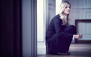 female in black long-sleeved dress sitting beside white wooden door frame