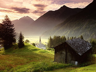 brown wooden house on grass field near mountain