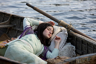 woman wearing teal dress sleeping on brown canoe on sea during daytime