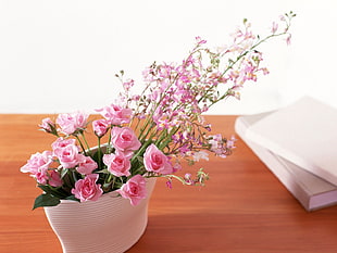 pink-petaled flowers in white ceramic pot on top of brown wooden table