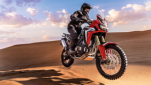 man riding red dirt bike on desert at daytime