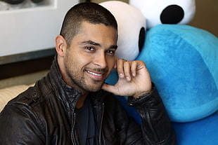 man in black leather zip-up jacket near the blue and white plush toy
