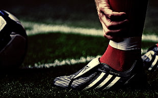 photography of person in black-and-white Adidas cleats near soccer ball