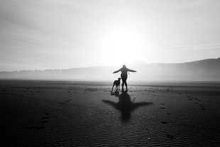 silhouette of woman and dog walking on desert under the sun
