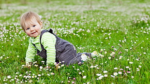 baby in gray overall pants and green long-sleeved shirt on grass