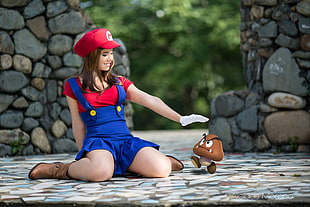shallow focus photography of smiling woman in Mario costume sitting on floor