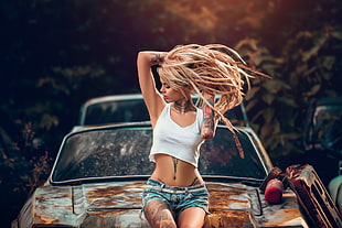 woman wearing white crop top and blue shorts sitting on hood of car