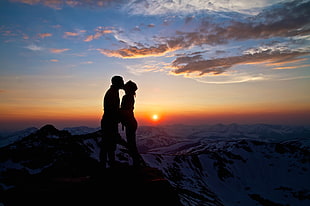 silhouette of man and woman kissing on mountain cliff